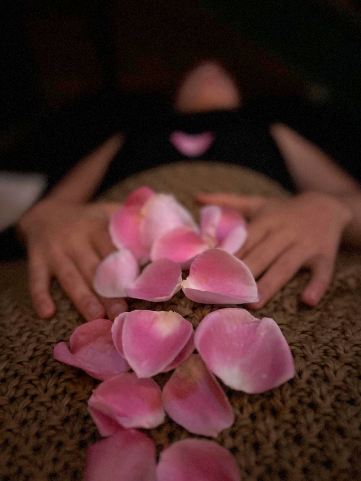 Hands resting over rose petals on a woven surface